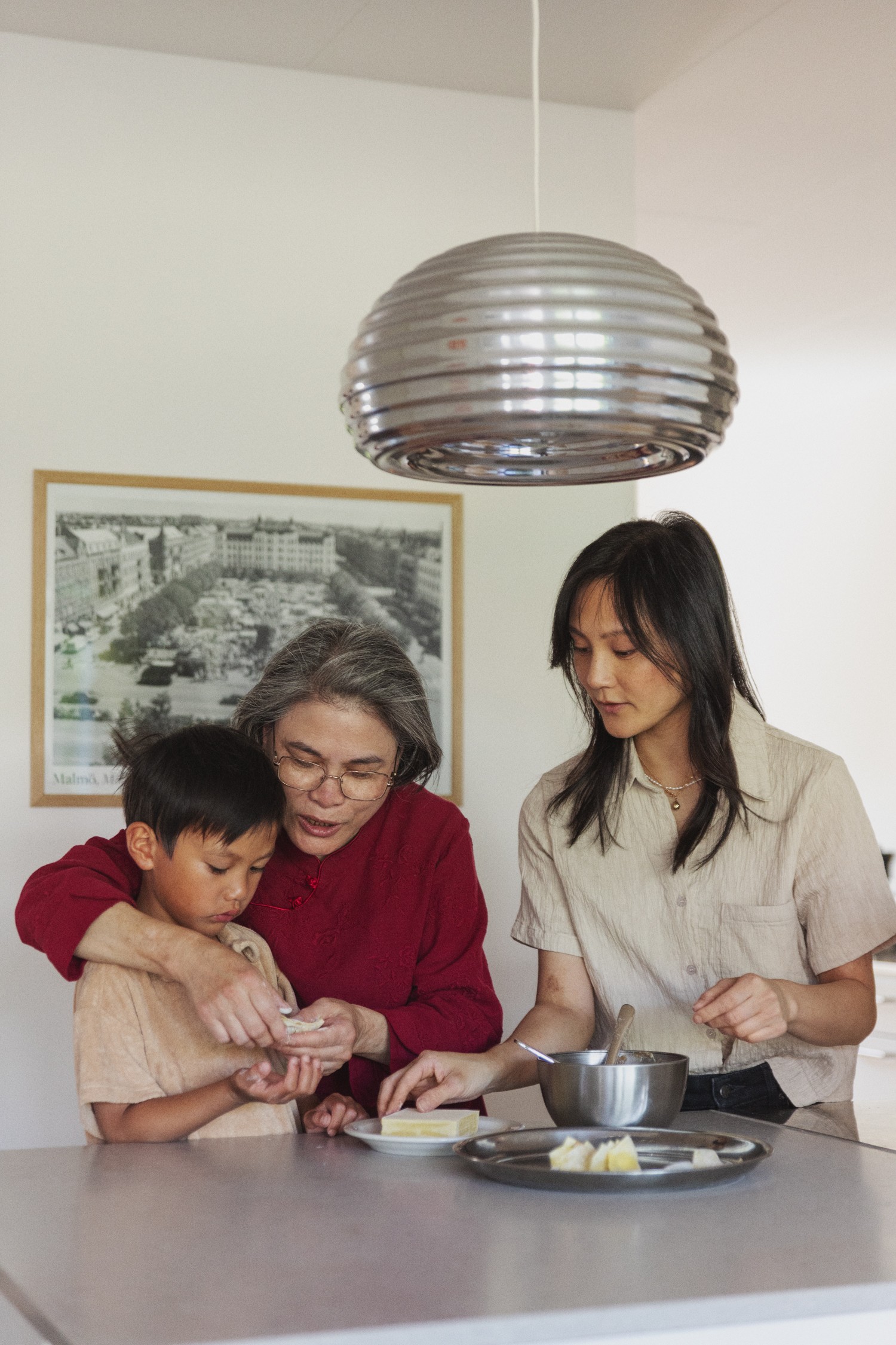 Grandmother, mother, and son cooking together in a kitchen, standing close and talking.