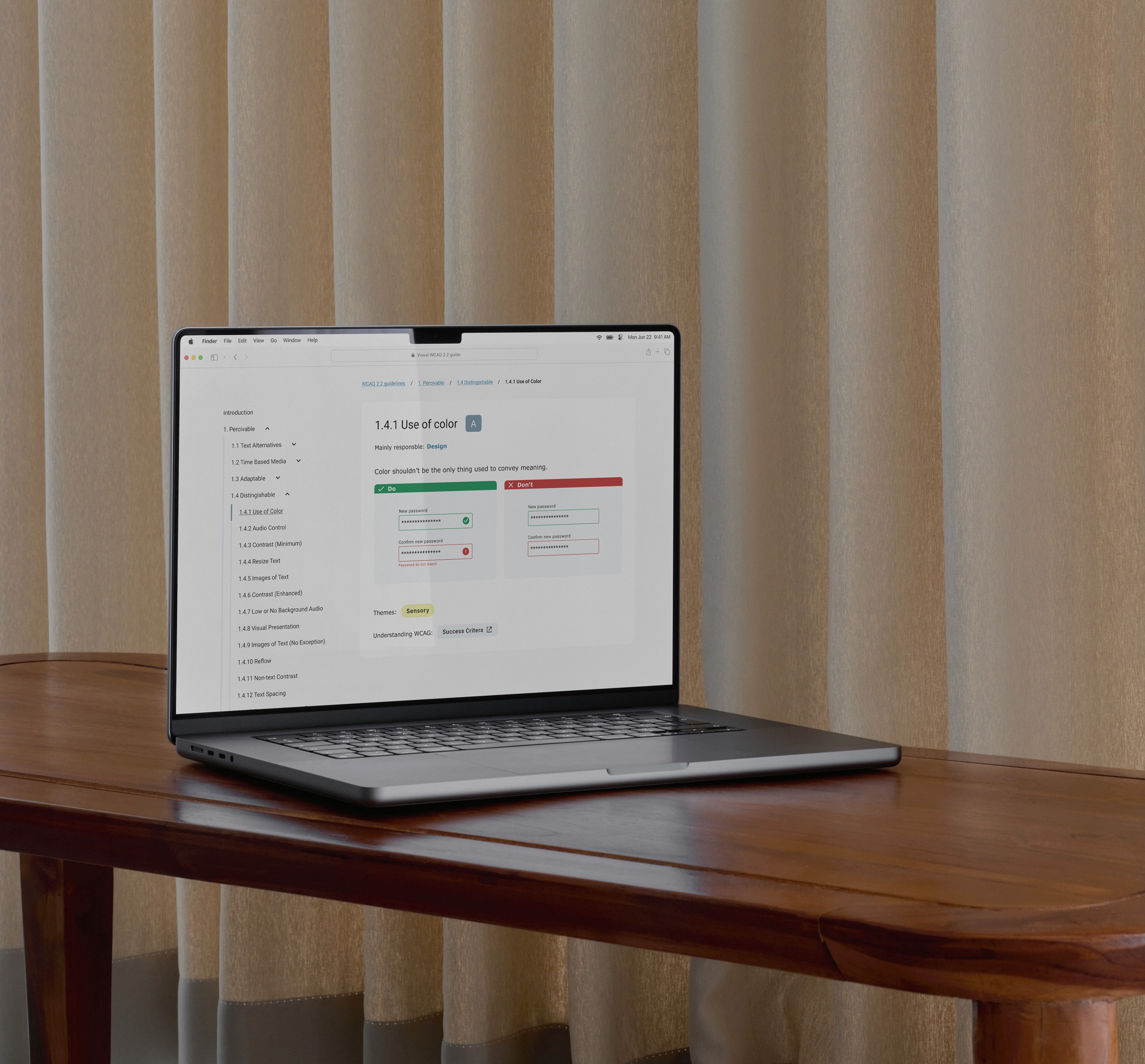Macbook displaying a design, placed on a wooden table with beige curtains in the background.
